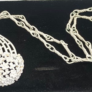 May include: A silver necklace with a flower-shaped pendant. The pendant is made of silver and has a delicate design. The necklace is on a black background.