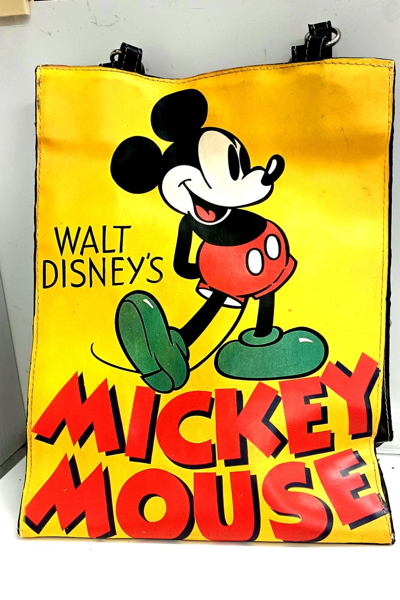 May include: Yellow tote bag featuring a smiling Mickey Mouse illustration. The bag has black handles and the words "WALT DISNEY'S" and "MICKEY MOUSE" in red. Mickey is depicted in his classic outfit with red shorts and green shoes.
