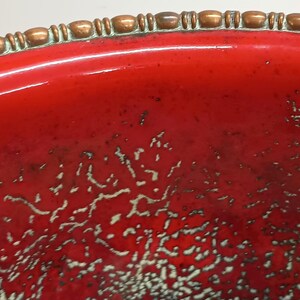 May include: A red ceramic bowl with a copper-coloured rim. The bowl has a speckled, textured surface.