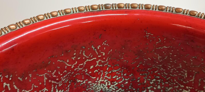 May include: A red ceramic bowl with a copper-coloured rim. The bowl has a speckled, textured surface.