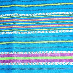 May include: A close-up of a blue fabric with horizontal stripes in various colors. The stripes include purple, green, yellow, and white, creating a vibrant and textured pattern. The fabric appears to be woven.