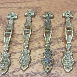 May include: Seven ornate brass door pulls with a decorative design. The pulls have a long, narrow shape with a curved handle and a pointed end.