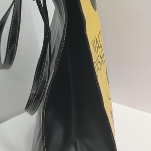 May include: Black tote bag with a yellow side panel featuring a cartoon design and the text "WALT DISNEY". The bag has black handles and white stitching.