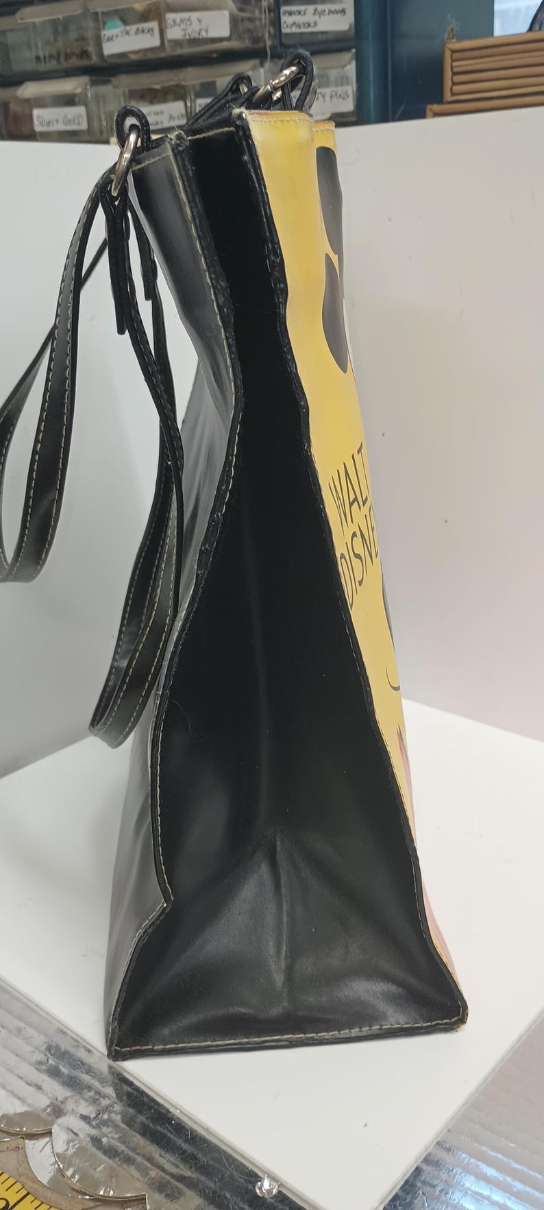 May include: Black tote bag with a yellow side panel featuring a cartoon design and the text "WALT DISNEY". The bag has black handles and white stitching.
