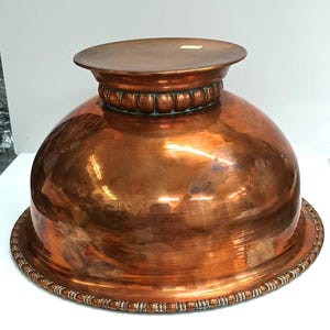 May include: A large copper bowl with a raised rim and a beaded design around the top and bottom. The bowl is polished and has a shiny finish.