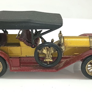 May include: A vintage toy car with a black convertible top, gold body, and maroon fenders. The car has detailed wheels and a classic design, evoking a sense of nostalgia. The toy car is a collectible item.