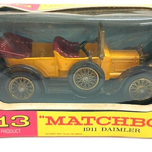 May include: A vintage Matchbox Y-13 1911 Daimler toy car in its original box. The die-cast model is yellow with maroon seats and a spare tire. The box is red and yellow with the Matchbox logo and product details.
