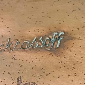 May include: Close-up of a copper surface with the inscription "Nekrassoff" etched into the metal.