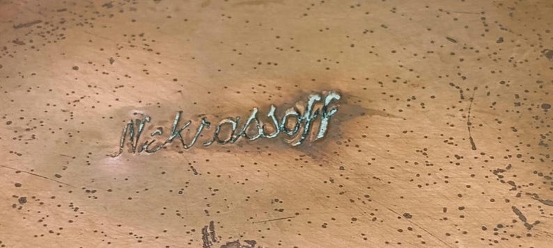 May include: Close-up of a copper surface with the inscription "Nekrassoff" etched into the metal.