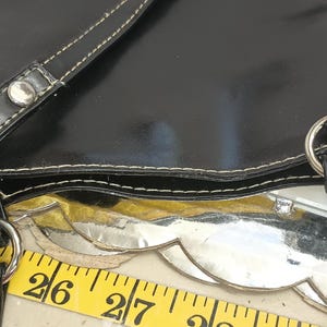 May include: Black tote bag with white stitching and silver hardware. The bag has two straps with silver rivets and metal rings. A yellow measuring tape is visible, showing measurements in inches.