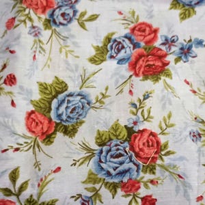 May include: White fabric with a repeating pattern of red and blue roses. The roses are surrounded by green leaves and small white flowers.