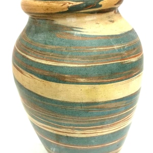 May include: A ceramic vase with a wide base and a narrow neck. The vase features horizontal stripes in teal, tan, and brown. The rim is a darker tan color. The vase is a decorative item.