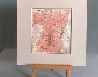 May include: A vintage map of Montreal, Canada, printed on cream paper and framed in a white mount. The map shows the city's streets and landmarks in red and black ink.