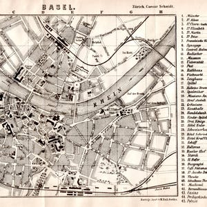 May include: A black and white vintage map of Basel, Switzerland, featuring the Rhine river, a grid system with letters A-H and numbers 1-6, and a numbered index of landmarks on the right side. The text includes Basel, Rhein, and Schmidt's Reisebücher.
