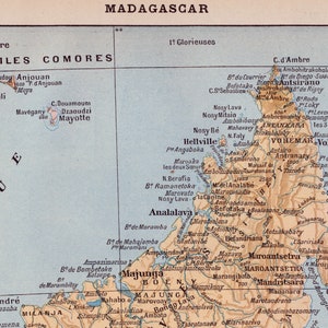 May include: A vintage map of Madagascar, a large island off the coast of Africa, with the surrounding islands of the Comoros. The map is printed on a light blue background with brown lines and text. The map shows the island's major cities, rivers, and mountains.