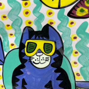 May include: A blue cat wearing yellow goggles with green lenses sits on a turquoise chair. The cat has black stripes and a white face. The background is a white and green pattern with yellow dots.