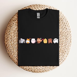 Könnte beinhalten: Schwarzes T-Shirt mit einer Reihe süßer Comic-Tiere, die verschiedene Outfits tragen. Zu den Tieren gehören ein Koala, ein Hamster, eine Katze, ein Eichhörnchen, ein Küken, ein Bär und ein Kaninchen.