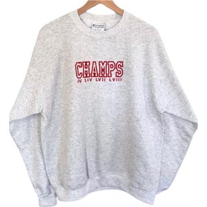 May include: Gray Champion sweatshirt with red embroidered text that reads "CHAMPS IV LIV LVII LVIII".