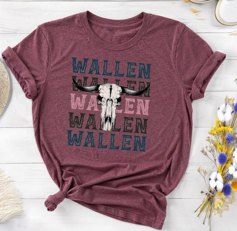 K&ouml;nnte beinhalten: Burgunderfarbenes T-Shirt mit umgekrempelten &Auml;rmeln. Es zeigt eine Grafik eines Bullensch&auml;dels und den Namen "WALLEN" in Blau, Rosa und Schwarz &uuml;bereinander. Das T-Shirt ist aus weichem Material. Das Design ist ein Statement.