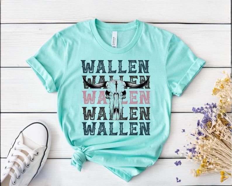 K&ouml;nnte beinhalten: Ein hellt&uuml;rkisfarbenes T-Shirt mit dem Wort "WALLEN", das viermal gestapelt ist, mit einer Bullensch&auml;del-Grafik in der Mitte. Das Wort "WALLEN" ist in Schwarz und Rosa gehalten. Ein wei&szlig;er Sneaker ist in der unteren linken Ecke zu sehen.