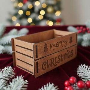 May include: A brown wooden Christmas crate with the words "merry Christmas" engraved on the front. The crate has a rectangular shape and a slatted design. A Christmas tree is engraved next to the word "merry".