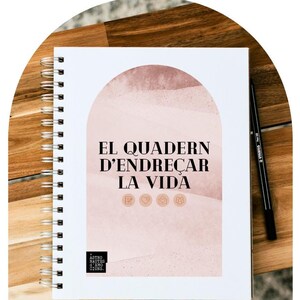 Può includere: Un quaderno bianco a spirale con il titolo "EL QUADERN D'ENDREÇAR LA VIDA" in nero. La copertina presenta un arco ad acquerello rosa con una texture sottile. Il quaderno è su una superficie di legno.