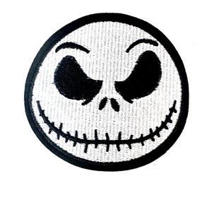 May include: Circular embroidered patch depicting Jack Skellington's face from The Nightmare Before Christmas. The design is black and white, with a black border. The patch has a stitched texture and a white background.