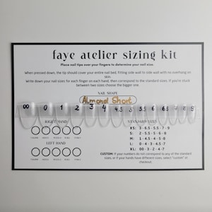 May include: A black and white Faye Atelier sizing kit with clear nail tips. The kit includes instructions for measuring nail sizes, with sizes ranging from 00 to 9. The nail shape is Almond Short.