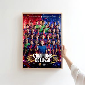 May include: A framed poster featuring a soccer team in blue and red uniforms, celebrating a victory. The poster has the words "CAMPIONS DE LIGA" and "FORCA BARCA!" with the years 2025 and 2026. The poster is held by a person.