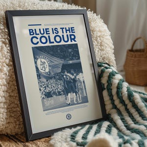 May include: A framed poster with a blue and white color scheme. The poster features a photo of a crowd of people at a sporting event, with the text "BLUE IS THE COLOUR" at the top. The poster also includes the Chelsea Football Club logo.