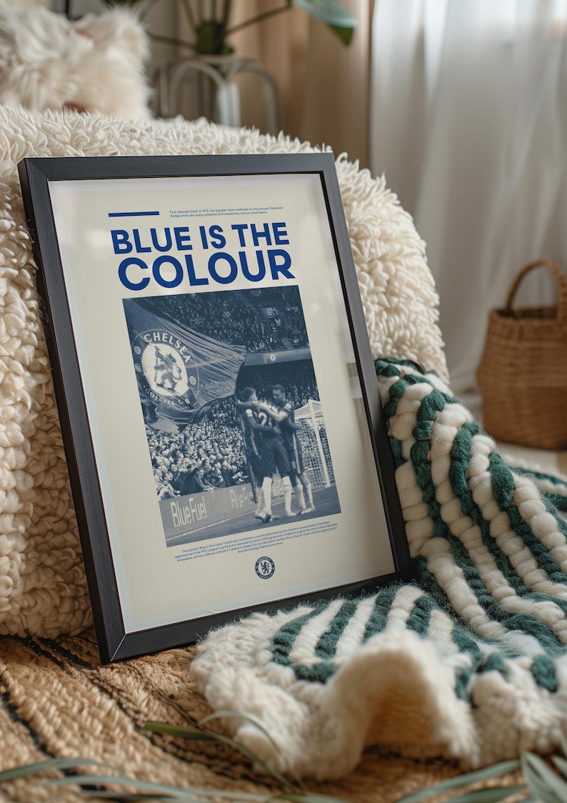 May include: A framed poster with a blue and white color scheme. The poster features a photo of a crowd of people at a sporting event, with the text "BLUE IS THE COLOUR" at the top. The poster also includes the Chelsea Football Club logo.