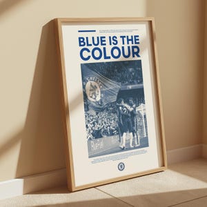 May include: A framed poster with a blue and white color scheme. The poster features a photo of a crowd of people at a soccer game, with the words "BLUE IS THE COLOUR" in large, bold letters at the top. The poster also includes the Chelsea Football Club logo.