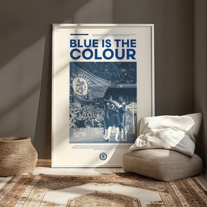 May include: A poster with a blue and white color scheme featuring a photo of two soccer players celebrating a goal. The poster has the text "BLUE IS THE COLOUR" at the top and the word "CHELSEA" in the photo.