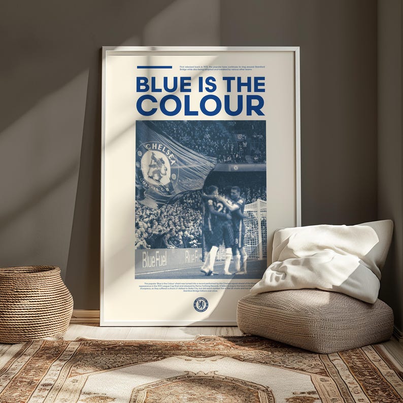 May include: A poster with a blue and white color scheme featuring a photo of two soccer players celebrating a goal. The poster has the text "BLUE IS THE COLOUR" at the top and the word "CHELSEA" in the photo.