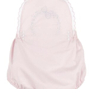 Könnte beinhalten: Hellrosa Baby-Strampler mit weißem, gewelltem Besatz und Trägern. Der Strampler hat eine gestickte Blumenverzierung auf der Vorderseite. Der untere Teil ist gerafft, hat eine Ballonform und wird mit Druckknöpfen geschlossen.