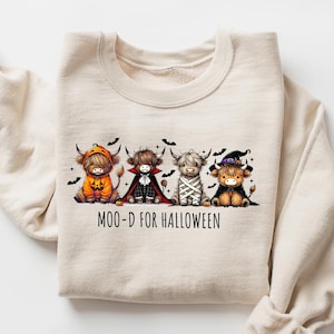 Könnte beinhalten: Cremefarbenes Sweatshirt mit einer Grafik von vier Highland-Kühen in Halloween-Kostümen. Die Kühe sind als Kürbis, Vampir, Mumie und Hexe verkleidet. Der Text "MOO-D FOR HALLOWEEN" steht darunter.