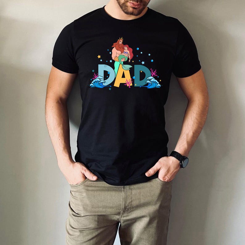 May include: Black t-shirt with a graphic of Ariel and King Triton from The Little Mermaid. The graphic says "DAD" with waves and sea life surrounding the letters.