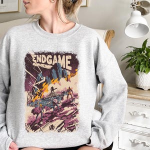 May include: A gray sweatshirt with a graphic print of a comic book cover featuring the text "ENDGAME" and characters from the Avengers movie.