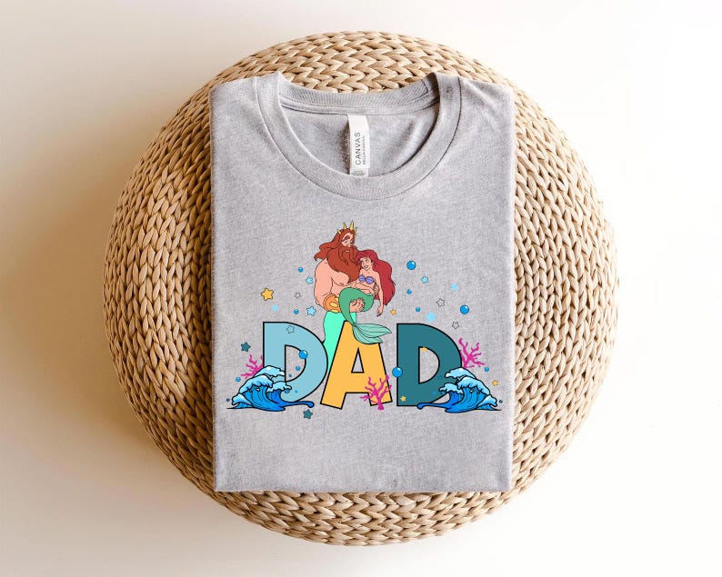 May include: Gray t-shirt with a graphic of King Triton and Ariel from The Little Mermaid. The graphic includes the word "DAD" with ocean waves and sea life.