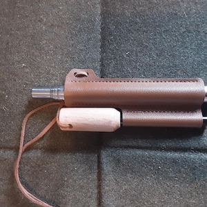 May include: A brown leather case with a wooden handle and a metal tube inside. The case has a strap for carrying.