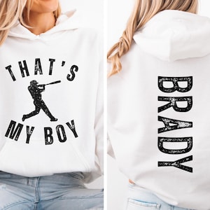 K&ouml;nnte beinhalten: Wei&szlig;er Hoodie mit einem Baseballspieler-Motiv und dem Text "That's My Boy" auf der Vorderseite und dem Namen "Brady" auf der R&uuml;ckseite.