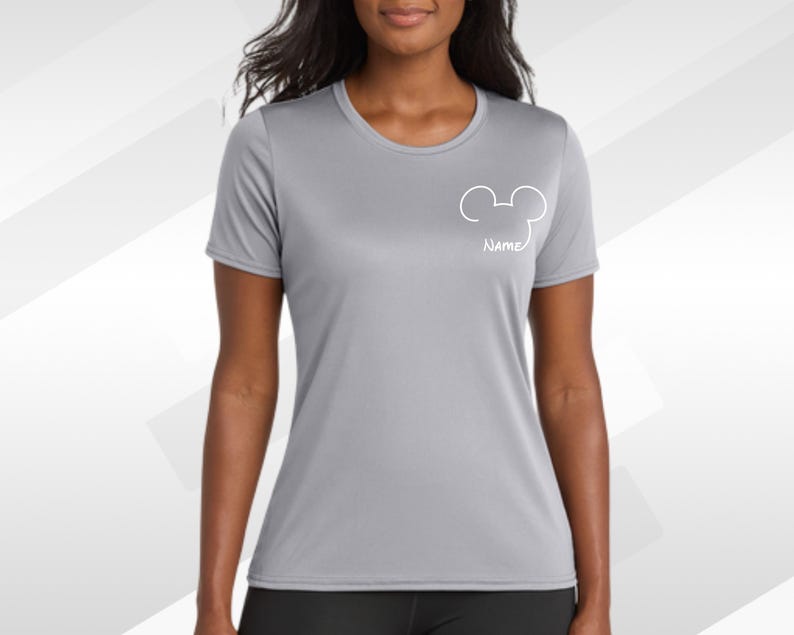 May include: A light gray athletic t-shirt with a white Mickey Mouse head outline and the word "Name" below it. The shirt has a crew neck and short sleeves. The background is a gradient of gray and white.