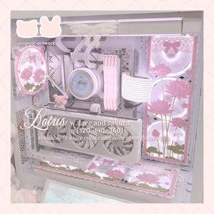 May include: A white computer case interior featuring pink lotus flower graphics, lace patterns, and a bow motif. The setup includes a liquid cooling block with a circular display, white RAM sticks, a graphics card, and illuminated fans with floral designs.