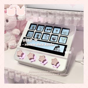 Puede incluir: Un stream deck blanco con un conjunto de cuatro perillas en forma de estrella. El deck presenta múltiples pantallas pequeñas que muestran imágenes de dibujos animados. El texto en el deck dice "star" y "set of 4 - stream deck knobs". El texto "keyboard version available" también es visible.