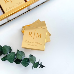 May include: Gold mirrored favor boxes with the initials "R M" and the text "Rubina & Mustafa September 2024" engraved on the front.