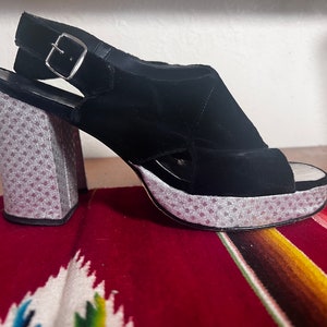 May include: Black velvet platform sandals with a silver polka dot pattern on the platform and heel. The sandals have a slingback strap with a silver buckle.