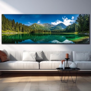 Könnte beinhalten: Panorama-Leinwanddruck einer ruhigen Bergsee-Szene. Das Kunstwerk zeigt einen lebendigen türkisfarbenen See, der die umliegenden grünen Bäume und die Bergkette unter einem strahlend blauen Himmel mit flauschigen weißen Wolken widerspiegelt. Der Druck wird über einem weißen Sofa angezeigt.