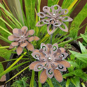 May include: Three metal flowers with intricate designs in a rusty brown color. The flowers are on metal stems and have a silver bead in the center of each flower.
