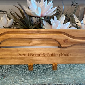 Puede incluir: Un juego de tabla de pan y cuchillo de corte de madera. La tabla marrón claro tiene un asa curva y una ranura para el cuchillo incluido. El texto "Bread Board & Cutting Knife" está grabado en la tabla. El cuchillo tiene un diseño floral.