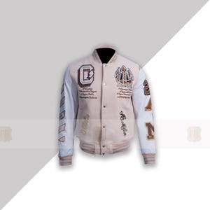 Könnte beinhalten: Eine weiße und braune Leder-Collegejacke mit gestickten Aufnähern und Text. Die Jacke hat einen weißen Kragen, weiße Ärmel und einen braunen Körper. Die Aufnäher beinhalten einen Buchstaben "C", einen Buchstaben "N", eine Zahl "2" und ein Wappen mit einem Dreizack. Der Text auf der Jacke beinhaltet "Mc. Milan" und anderen Text in einer Schreibschrift.